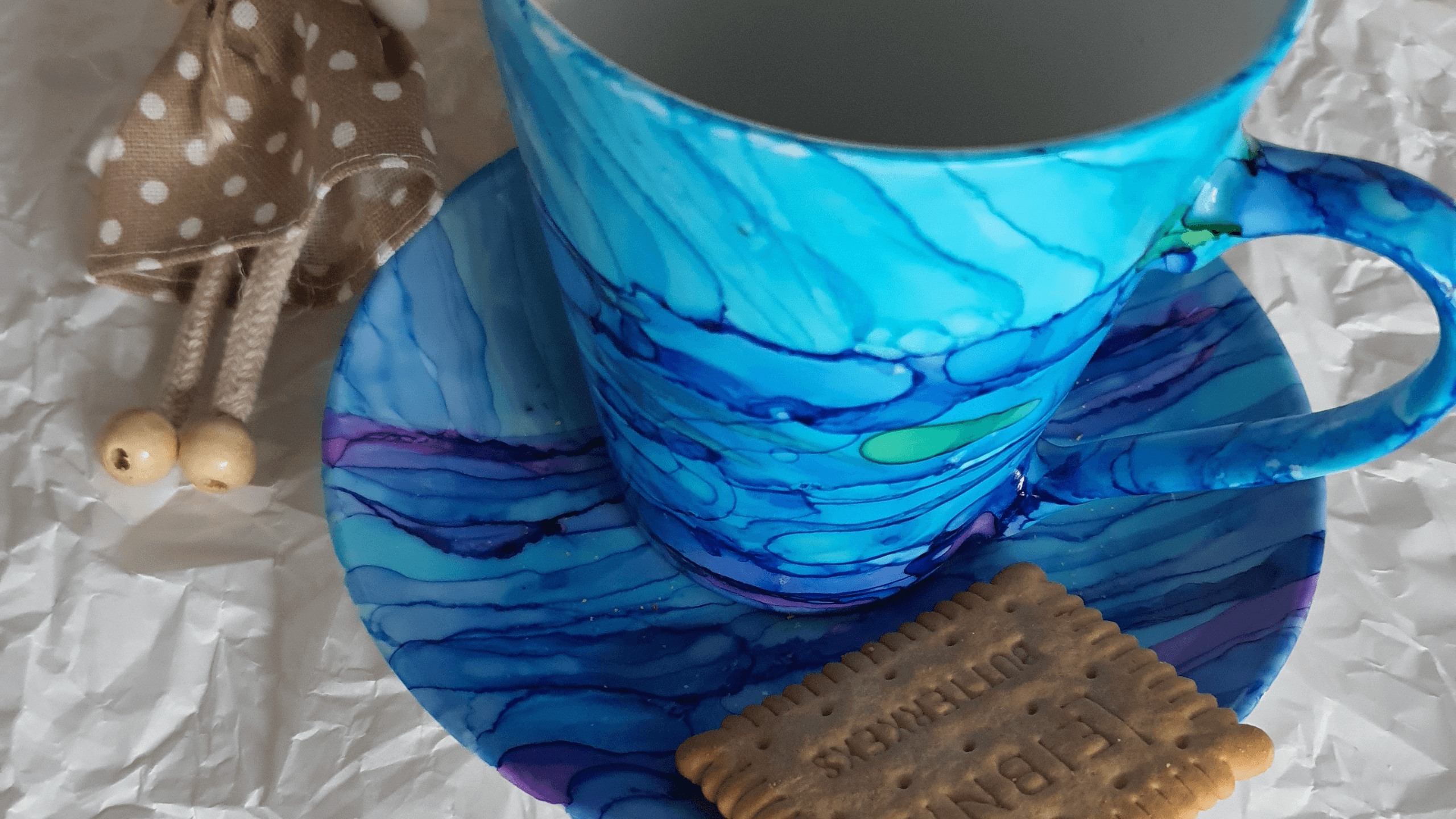 Ceramiczny kubek z podstawka i herbatnikiem, pomalowany na niebiesko tuszami