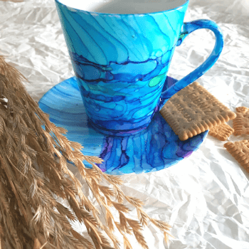 Ceramiczny kubek z podstawka i herbatnikiem, pomalowany na niebiesko tuszami